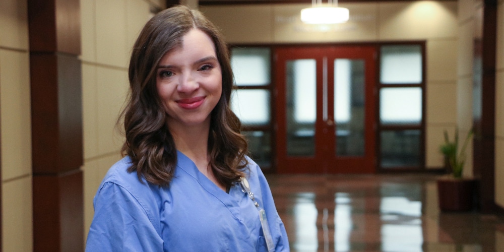 A woman in scrubs showcasing a passion for nursing, Dakota Babcock '19, standing in a hallway.