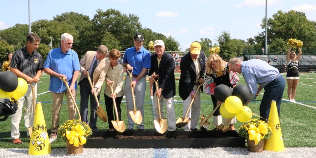 A group of people celebrating Duke Hall's groundbreaking with shovels in front of a football field.