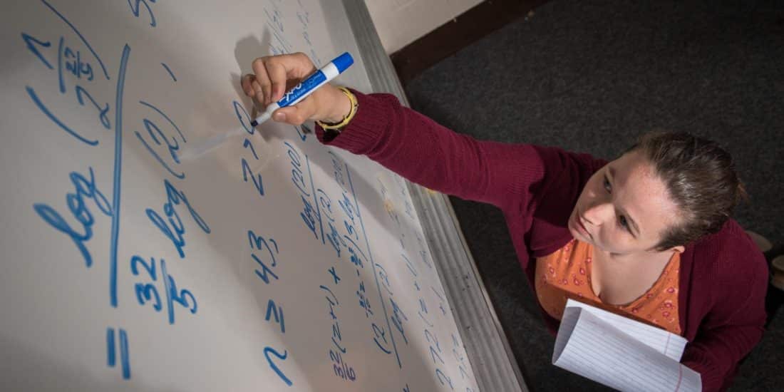 Faculty member writing mathematics equations on dry erase board.