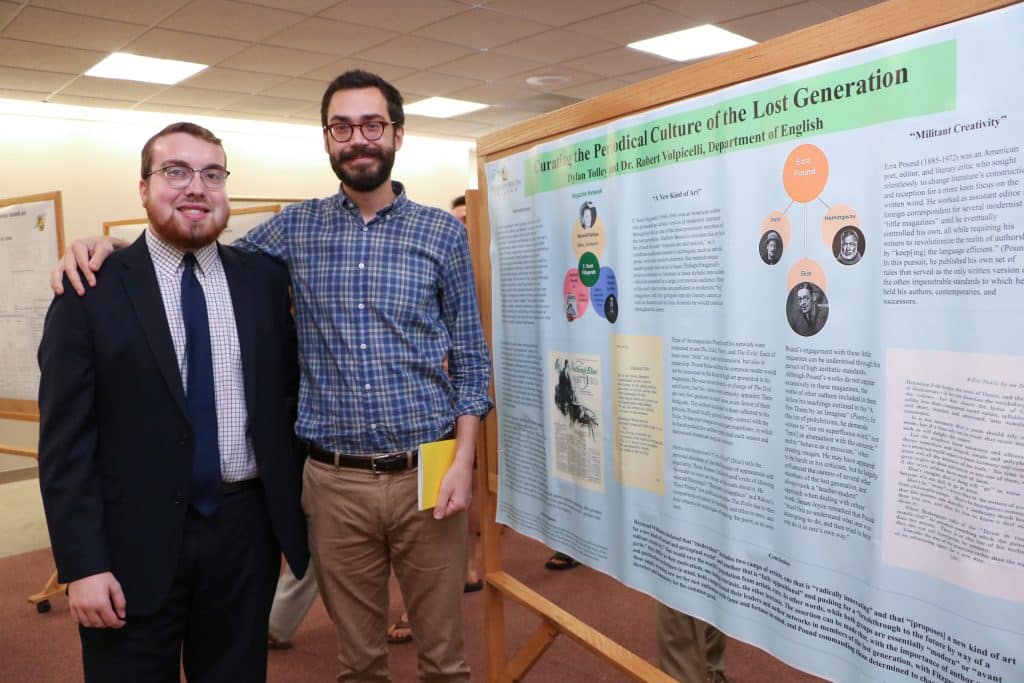 An English student and faculty member smile together with presentation research board