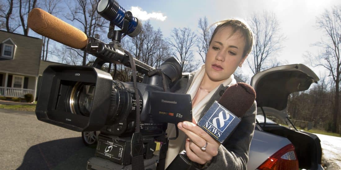 Student news reporter holding microphone while reviewing video camera footage