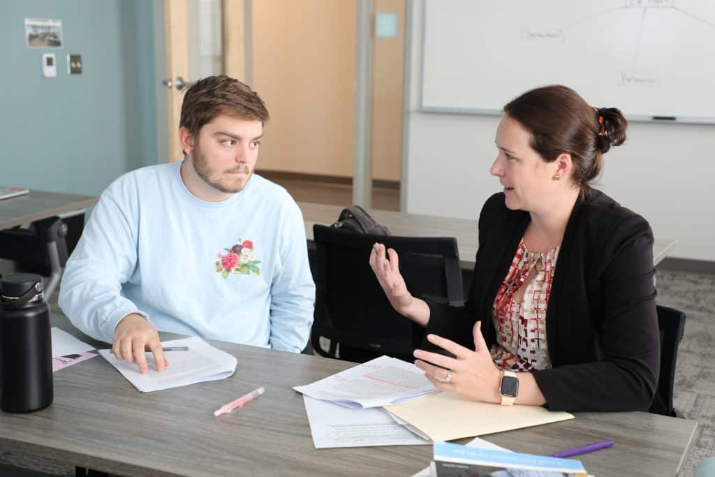 Education student and faculty member discuss coursework sitting at a table