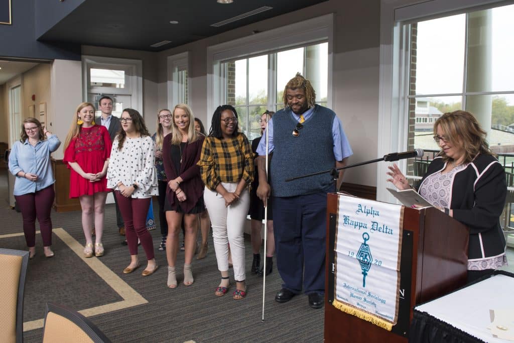 Students stand near a podium for induction into honor society