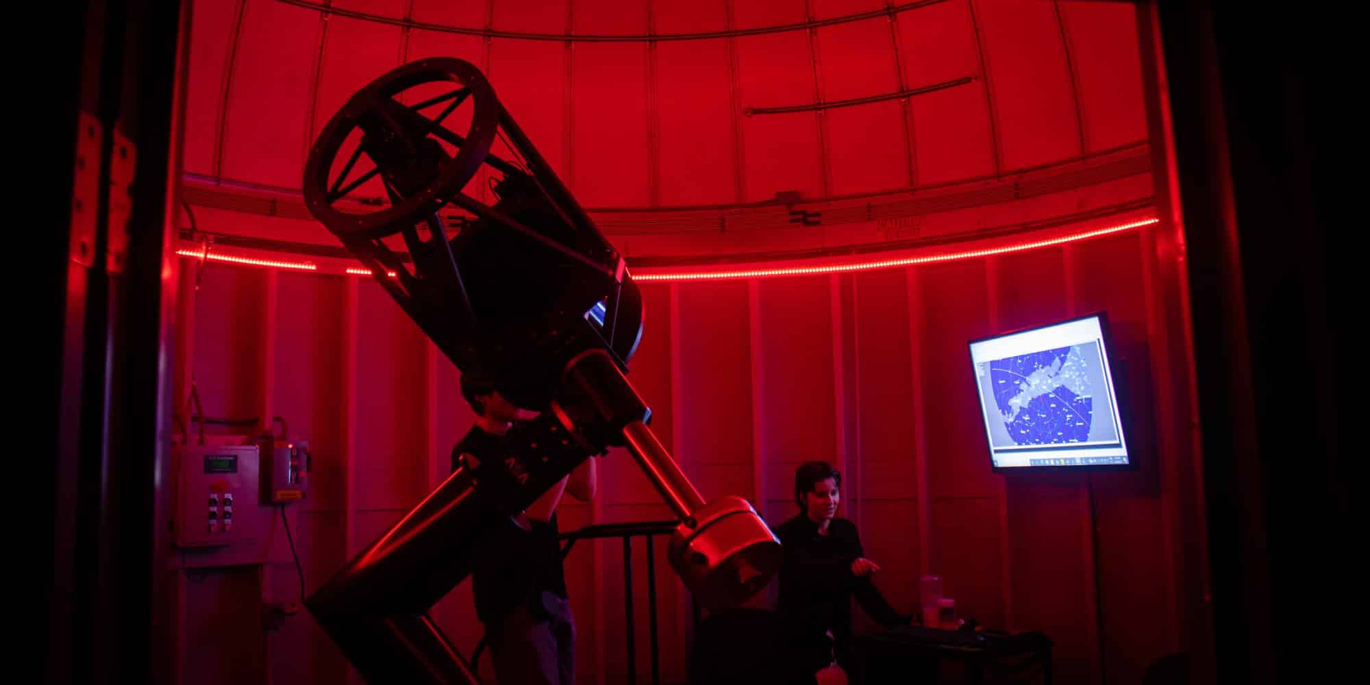 Red light fills the interior of the Keeble Observatory while a student views through the telescope