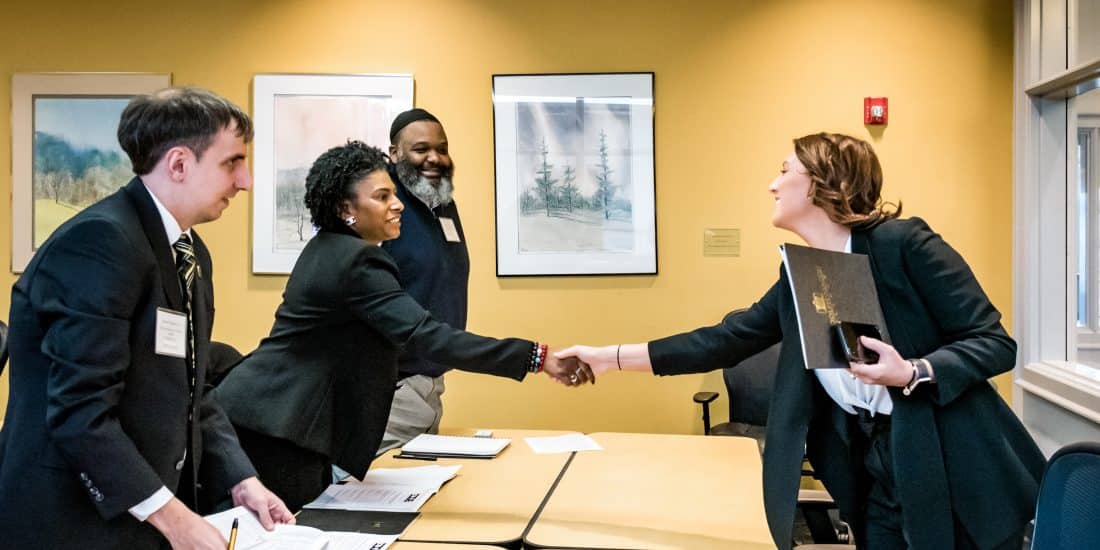 Students greet real-world clients by shaking hands over conference room table