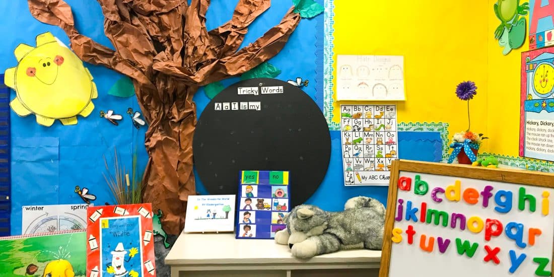 An cheery elementary school classroom featuring a teddy bear and a tree.
