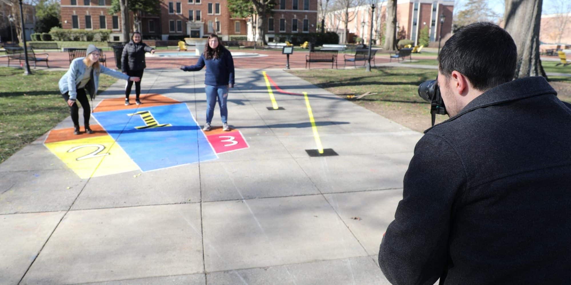 Student taking photo of three students standing near their 3D chalk artwork