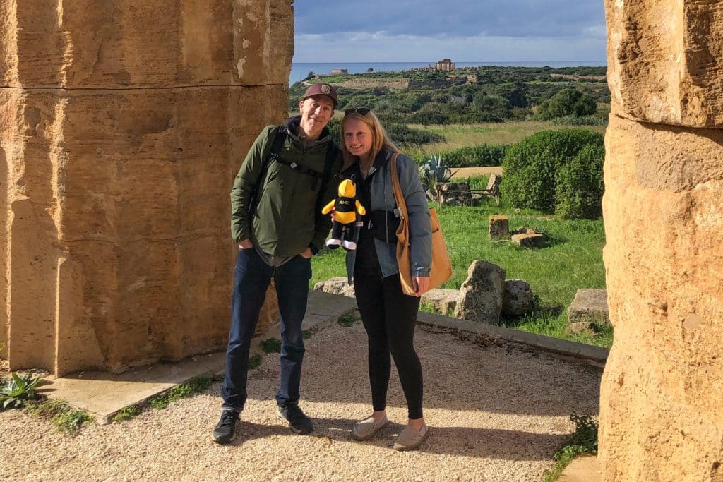 Two people standing near ancient ruins holding a stuffed yellow jacket
