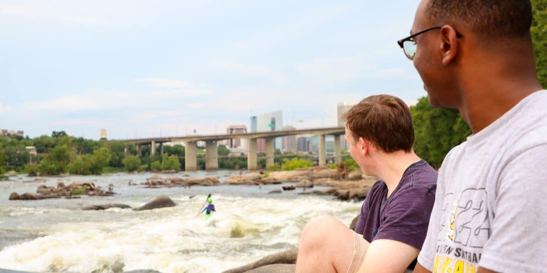 Students look towards the Richmond skyline while sitting at the James River
