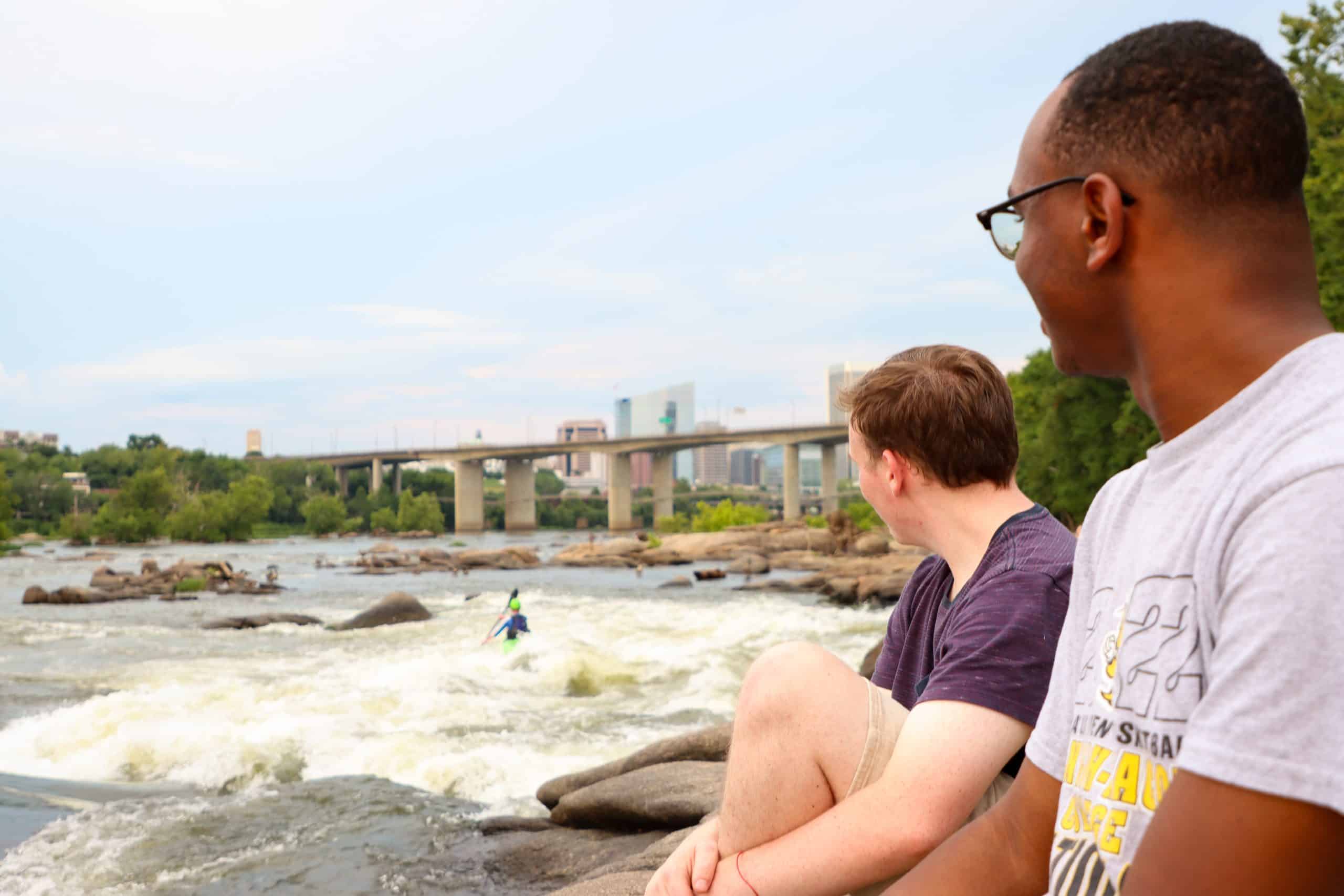 Students look towards the Richmond skyline while sitting at the James River