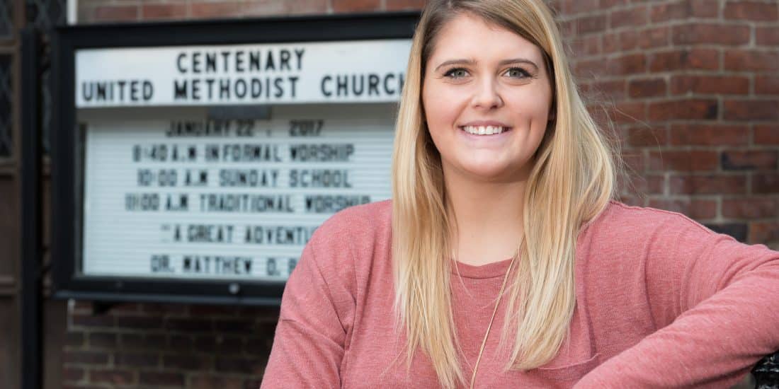 A RMC student smiles at the camera in front of the Centenary United Methodist Church sign where they interned