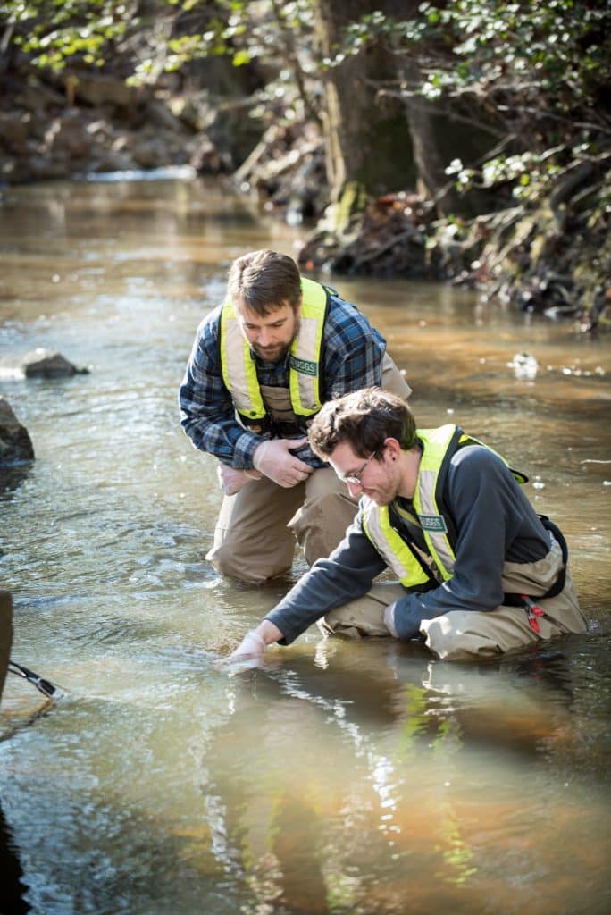 A RMC student an employer work together in a stream during an internship