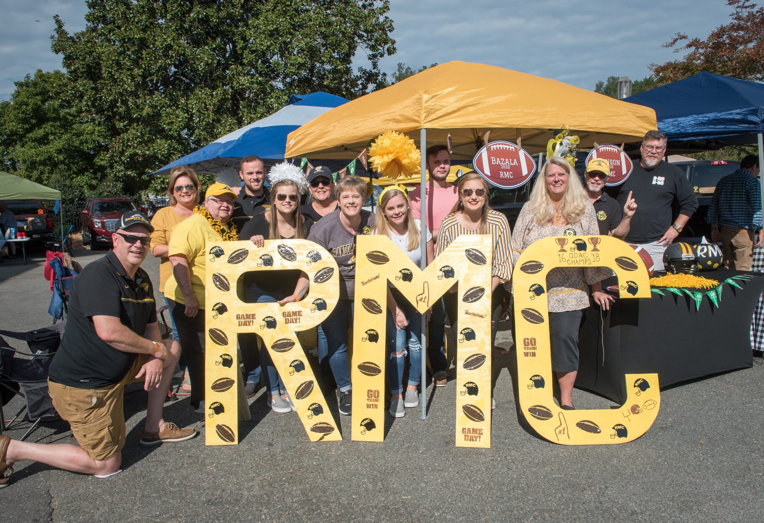 A group of alumni posing in front of a sign that says rmc.