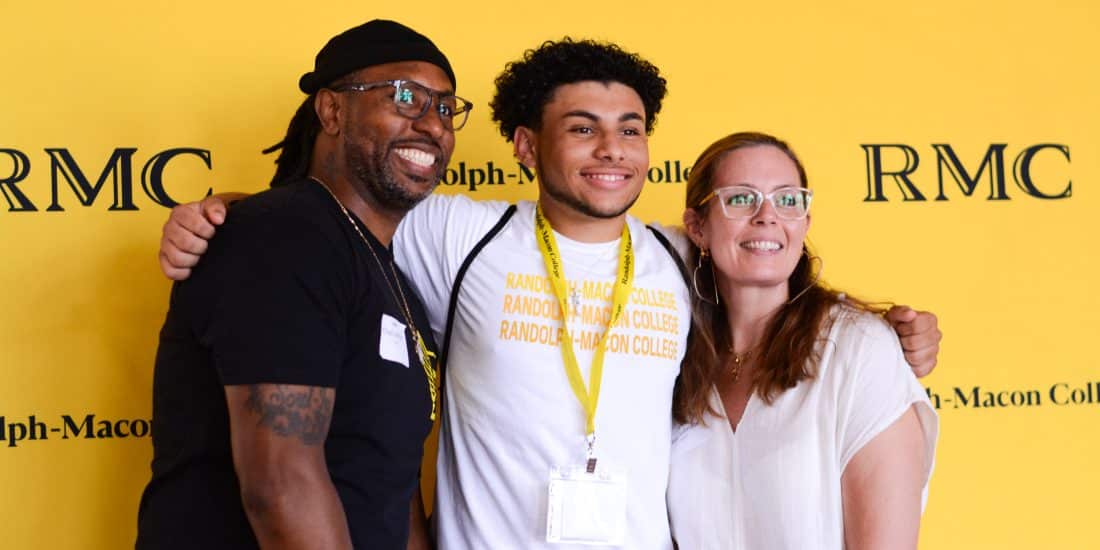 A RMC student and his parents stand in front of a yellow RMC step and repeat during Registration Day