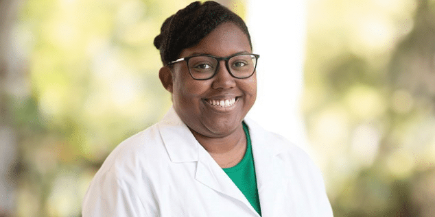 A black woman in a white lab coat smiling.