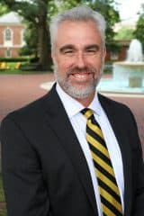 Jim Woods, a man in a black suit, wearing a yellow tie.