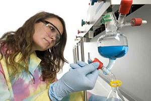 A student in a lab coat working with a beaker filled with a blue solution