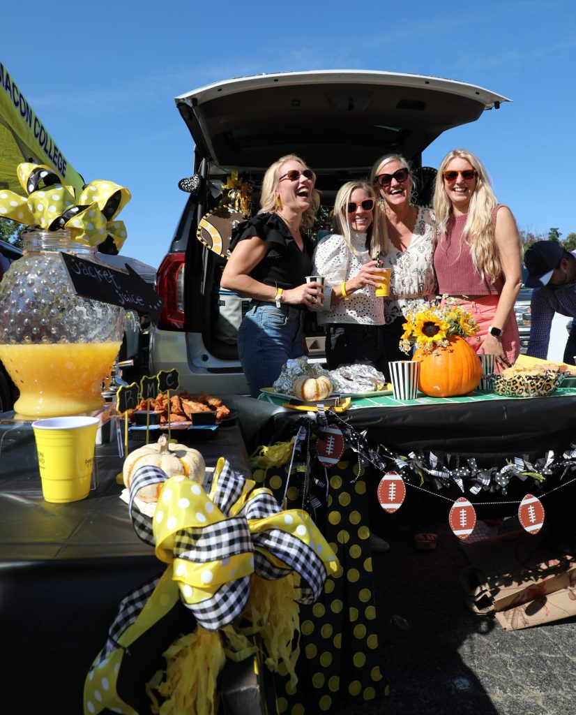 Four women pose at their tailgating set up during a football game