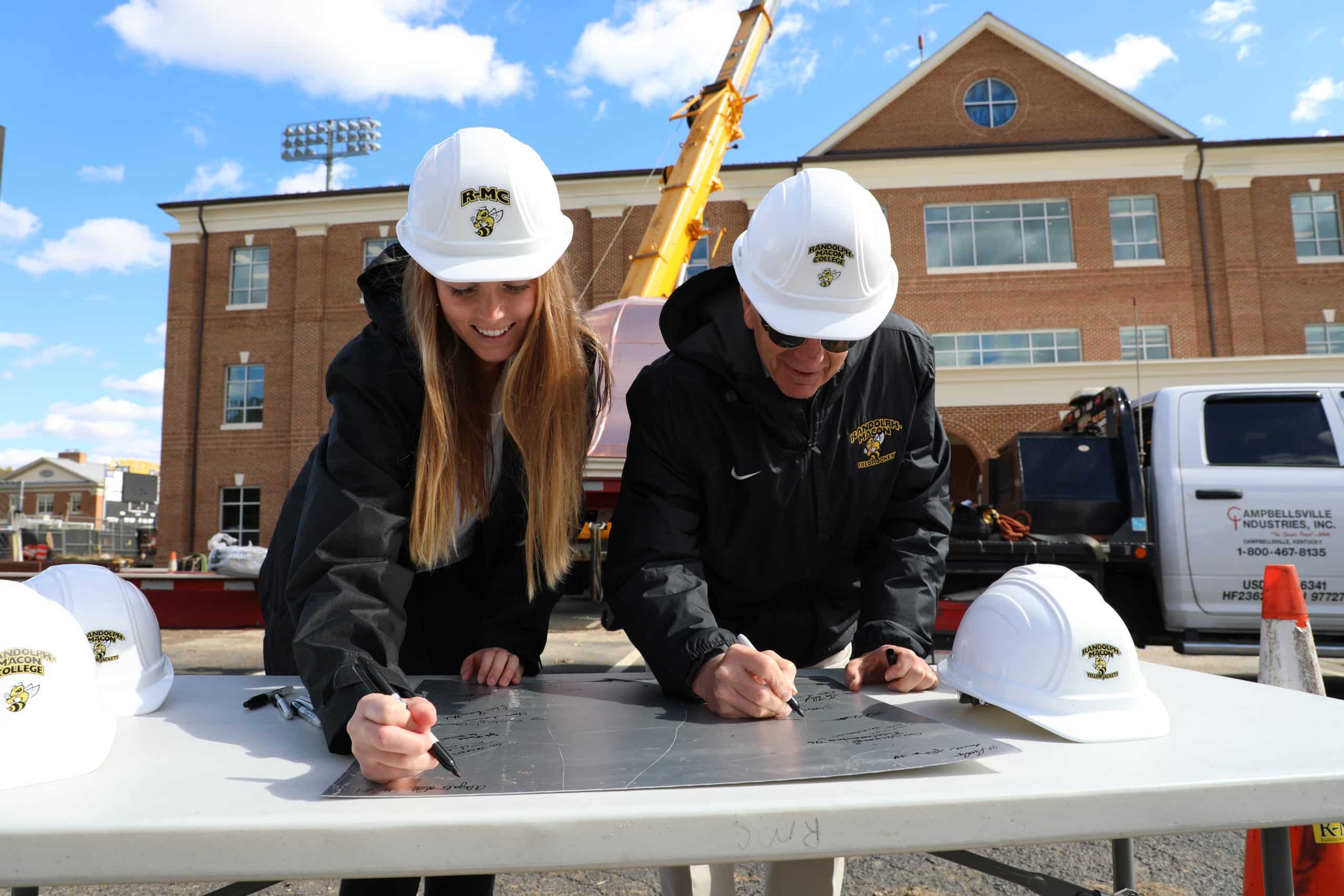 Two people in hard hats signing a piece of paper.