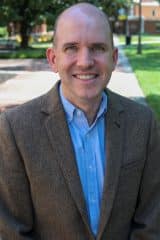 Brian D. Sutton, a bald man in a brown jacket, smiling.