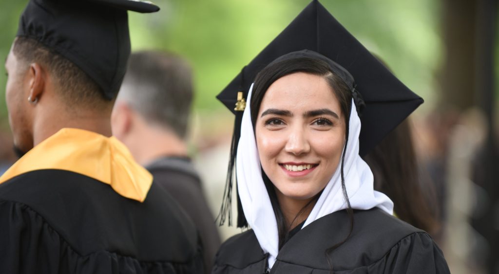 A RMC graduate in a headscarf and regalia smiles at the camera during commencement