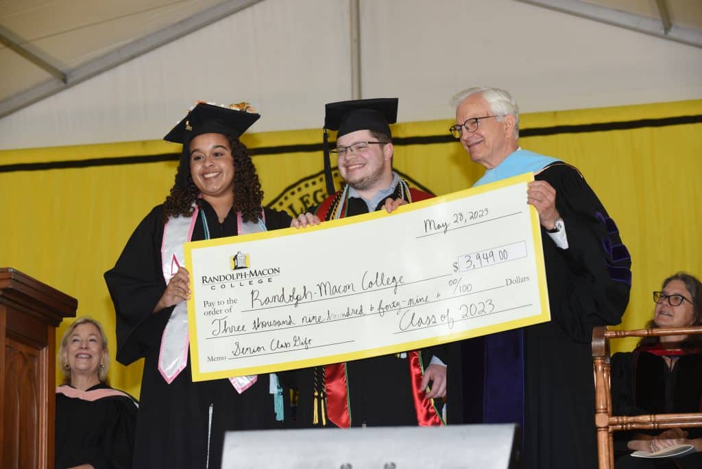 Two students and President Lindgren pose with a giant check during commencement.