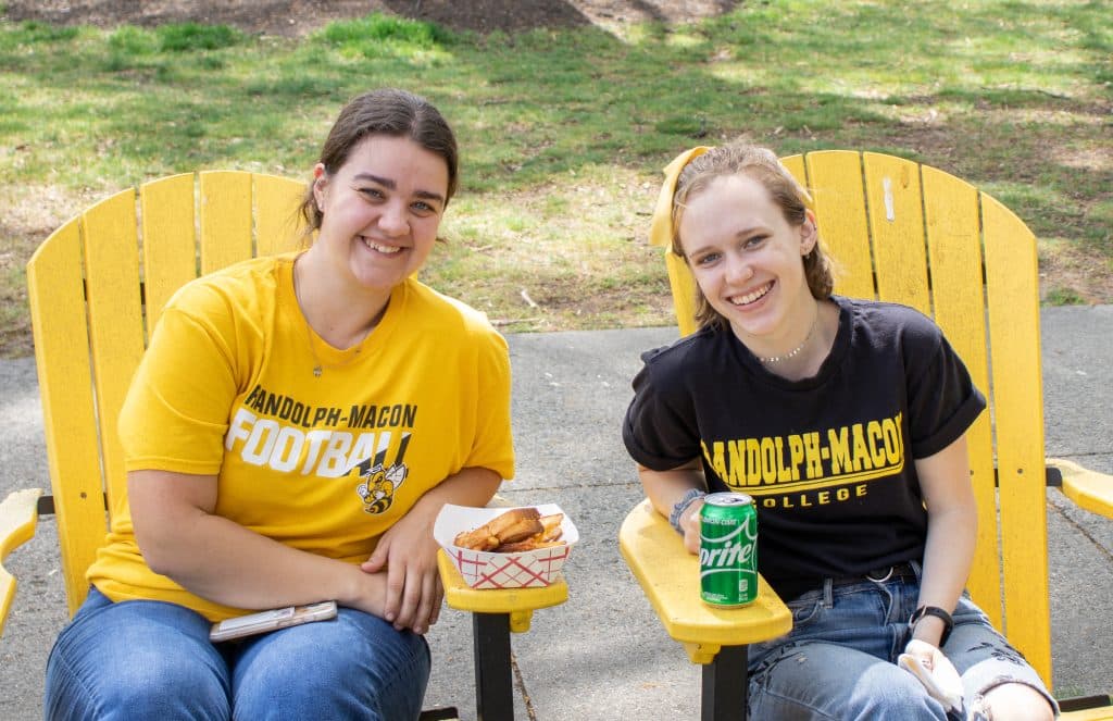 Two RMC students smile for the camera while sitting in yellow Adirondack chairs 