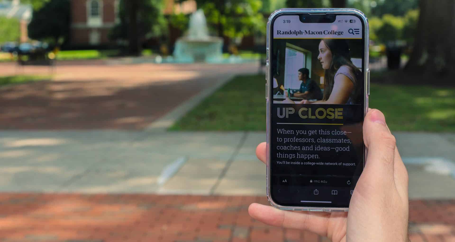A person holding up a cell phone with the newly redesigned RMC website displayed