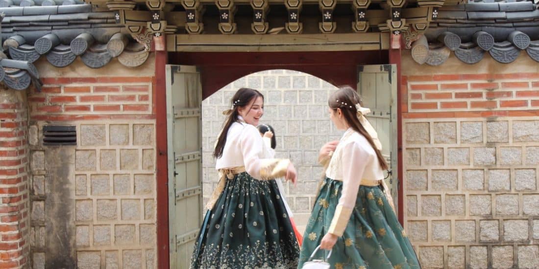 Two women in traditional korean dress walking through an archway.