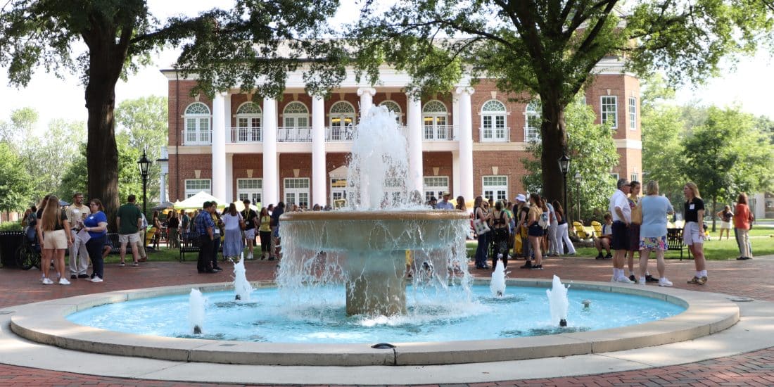A fountain in front of a building with people attending admitted student events around it.