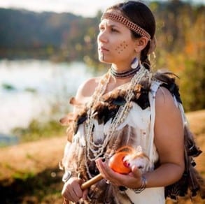 Raven Custalow, dressed in a Native American costume, holding an apple, captivates the audience with her mesmerizing performance.