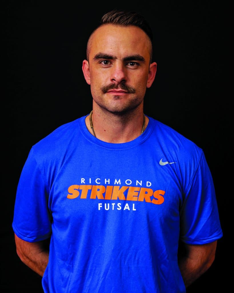 Man with a mustache wearing a blue "richmond strikers futsal" t-shirt against a black background.
