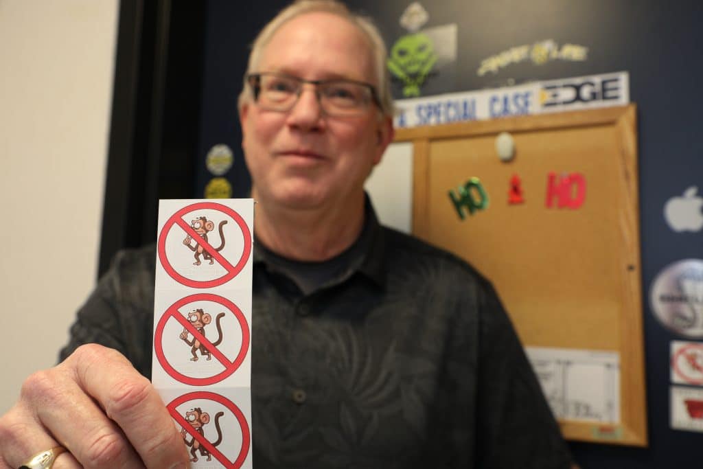 A man holding a strip of stickers with the the phrase "no code monkeys" in an office setting.