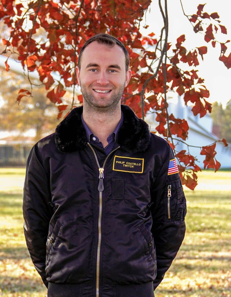 Man smiling outdoors with autumn leaves in the background.