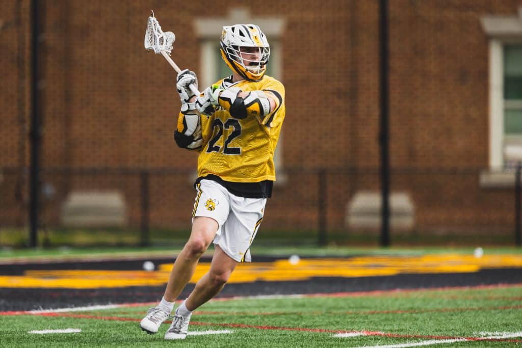 Lacrosse player in yellow jersey number 22 cradling the ball during a game.