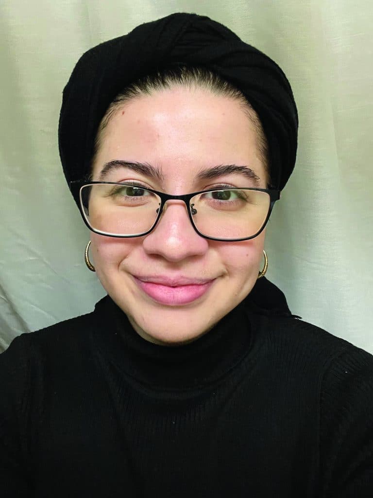 A person with a black headwrap and glasses smiling at the camera.