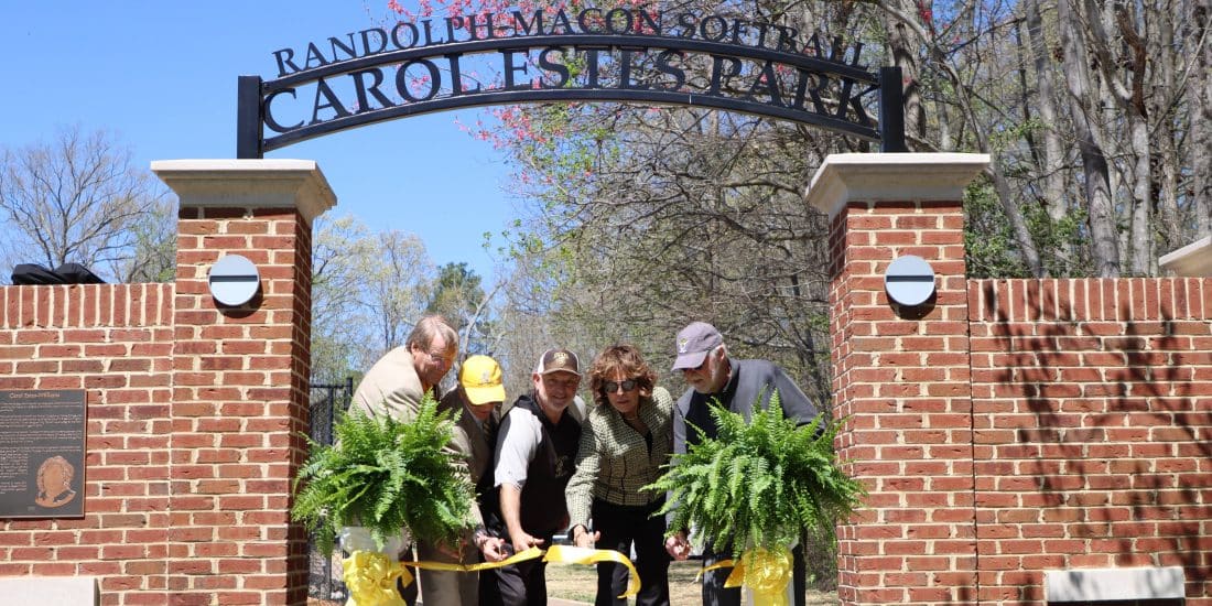 Five people participating in a ribbon-cutting ceremony at the entrance of randolph-macon college's caroline park.