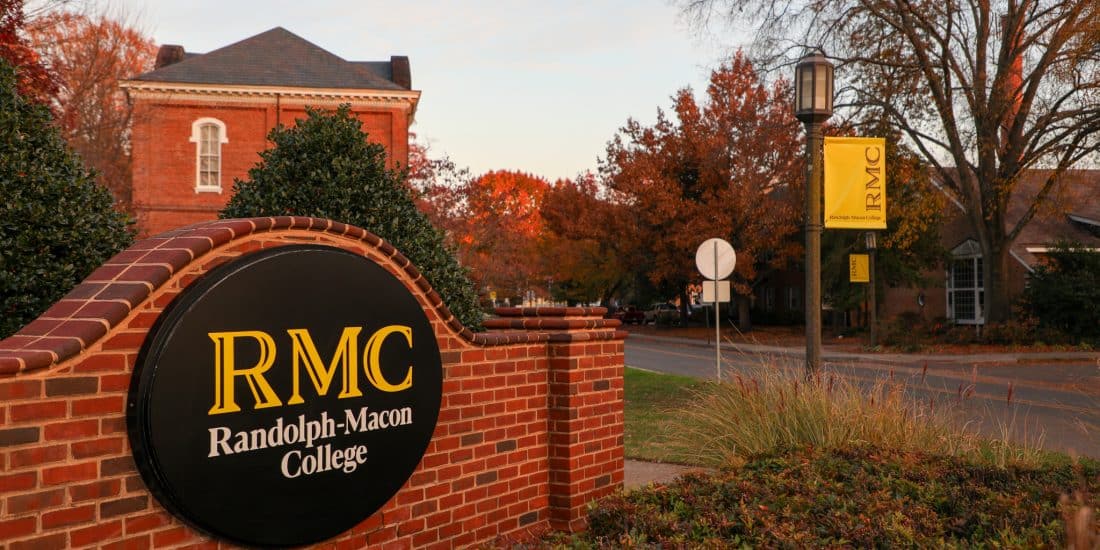 Entrance sign of randolph-macon college with a brick backdrop and autumn foliage.
