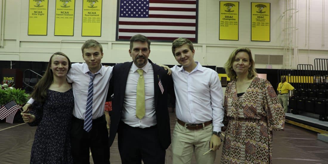 A family of five posing in a gymnasium with american flag and yellow banners hanging in the background.