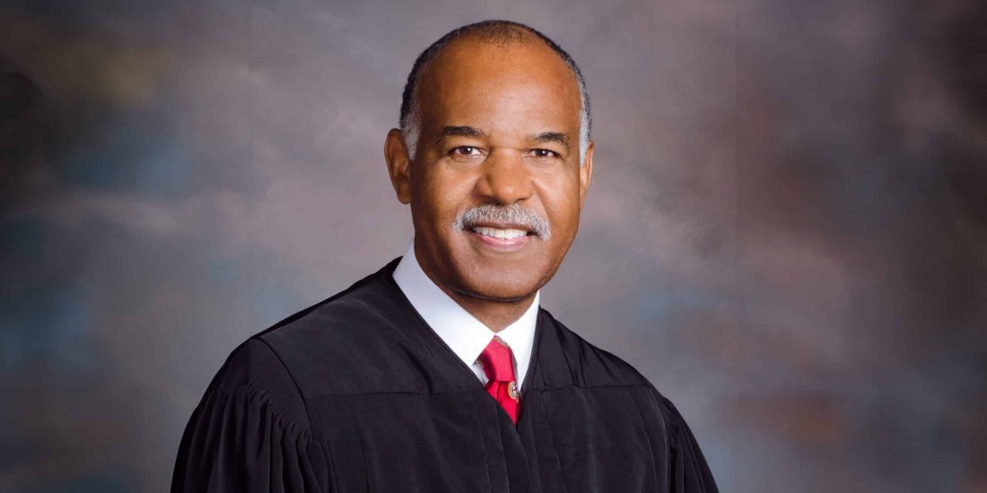 Roger Gregory in judicial robes posing for a formal portrait with a mottled background.